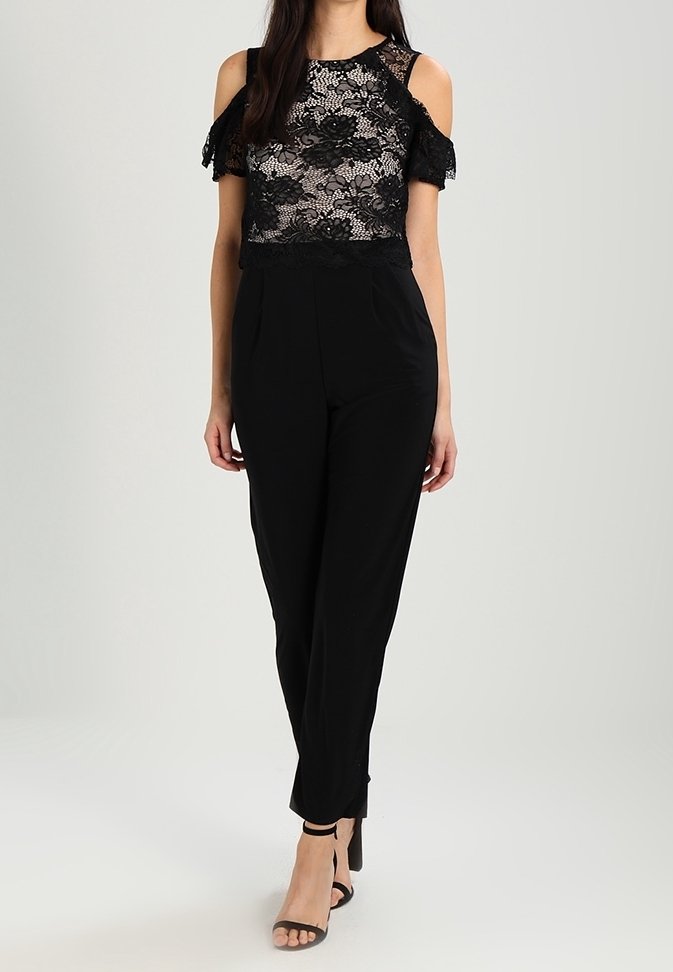 Czarna koronkowa bluzka z odkrytymi ramionami, wzory kwiatowe, połączona z czarnymi spodniami o wysokim stanie i straponami na wysokim obcasie.