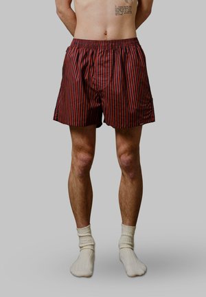 Shorts rayés rouge et marine avec une taille élastique. Portés avec des chaussettes de cheville côtelées de couleur crème. Accent sur la texture du tissu des shorts.