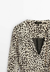 Robe portefeuille imprimé léopard avec un décolleté plongeant en V, des manches longues et une taille cintrée. Réalisée dans un tissu léger aux tons crème et noir.