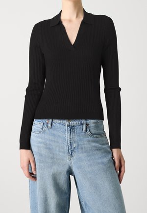 Musta ribbed-hihainen paita, jossa on V-pääntie ja kaulus, yhdistettynä vaaleansinisiin löysiin farkkuihin, jotka esittelevät tekstuurista kangasta.