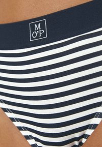 Bas de bikini rayé avec des rayures horizontales bleu marine et blanches, en tissu doux, et une étiquette logo au niveau de la taille.