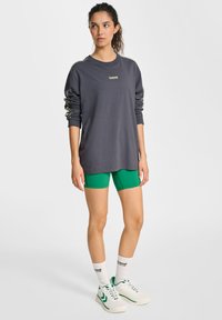 Långärmad grå t-shirt med logotyp och gröna detaljer; matchad med gröna träningsshorts. Vita strumpor och sneakers fulländar outfiten.