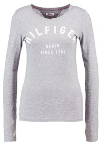 Ljust grå långärmad skjorta med "HILFIGER DENIM SINCE 1985" tryckt i vitt över bröstet, rund halsringning.