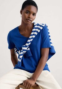 Kék, rövid ujjú póló, V-nyakkal, fehér és kék csíkos pulóverrel a vállakon. Zökkenőmentes textúra.