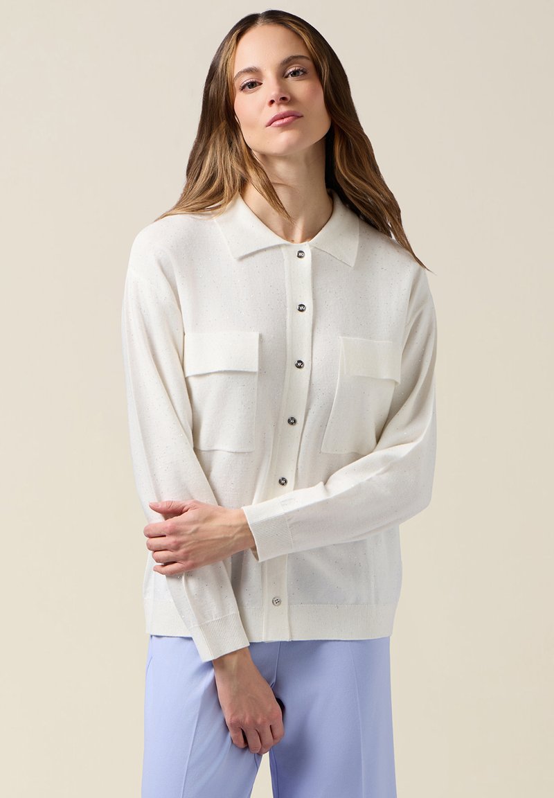 Cardigan bianco leggero con texture liscia, caratterizzato da collo a camicia, chiusura a bottoni e due tasche sul petto. Vestibilità sagomata.