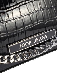 Pochette en simili cuir noir avec une texture crocodile. Équipée d'une chaîne argentée et d'une plaque logo en métal noir portant l'inscription "JOOP! JEANS."