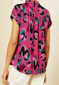 Lyhythihainen pusero kirkkaassa pinkissä, jossa rohkea musta ja vihreä eläinkuosi. Mallissa on kauluksen muotoinen pääntie ja rento istuvuus.