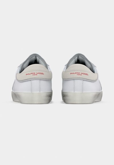 Paire de baskets basses blanches avec des languettes de talon grises, texte rouge "Philippe Model Paris", et semelles légèrement usées, vue de dos.