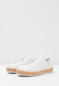 Vita lädersneakers med en texturerad korksula. Har en rund tå, snörning framtill och en slät yta utan synliga mönster eller detaljer.