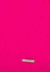 Jasnoróżowy sweter o miękkiej strukturze dzianiny, z małą metalową metką wszytą na dole. Prosty, okrągły dekolt.