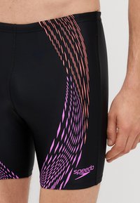 Črne kopalne hlače z dinamičnim vzorcem v rožnati in oranžni barvi, izdelane iz raztegljivega materiala. Na spodnji desni strani se nahaja logo Speedo.