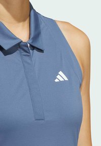 Gaiši zila bezpiedurkņu polo krekls ar apkakles izgriezumu, ar baltu Adidas logo kreisajā krūtī un gludu, elastīgu audumu.