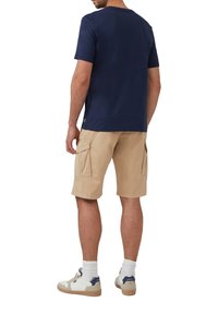 Marineblauwe katoenen t-shirt met een ronde hals, gecombineerd met beige cargoshorts met zakken, afgerond met witte en marineblauwe sneakers.