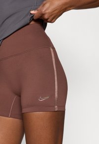 Καφέ αθλητικό σορτς με λείο ύφασμα, μεταλλικό λογότυπο Nike και αντίθετη επένδυση στην πλευρά.