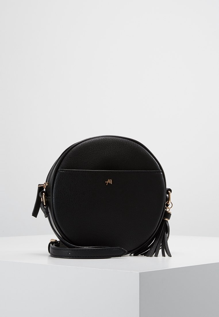 Kulatá černá kožená kabelka přes rameno se zlatými doplňky a střapcovým detailem. Hladká textura se zipem na zavření a nastavitelným popruhem.