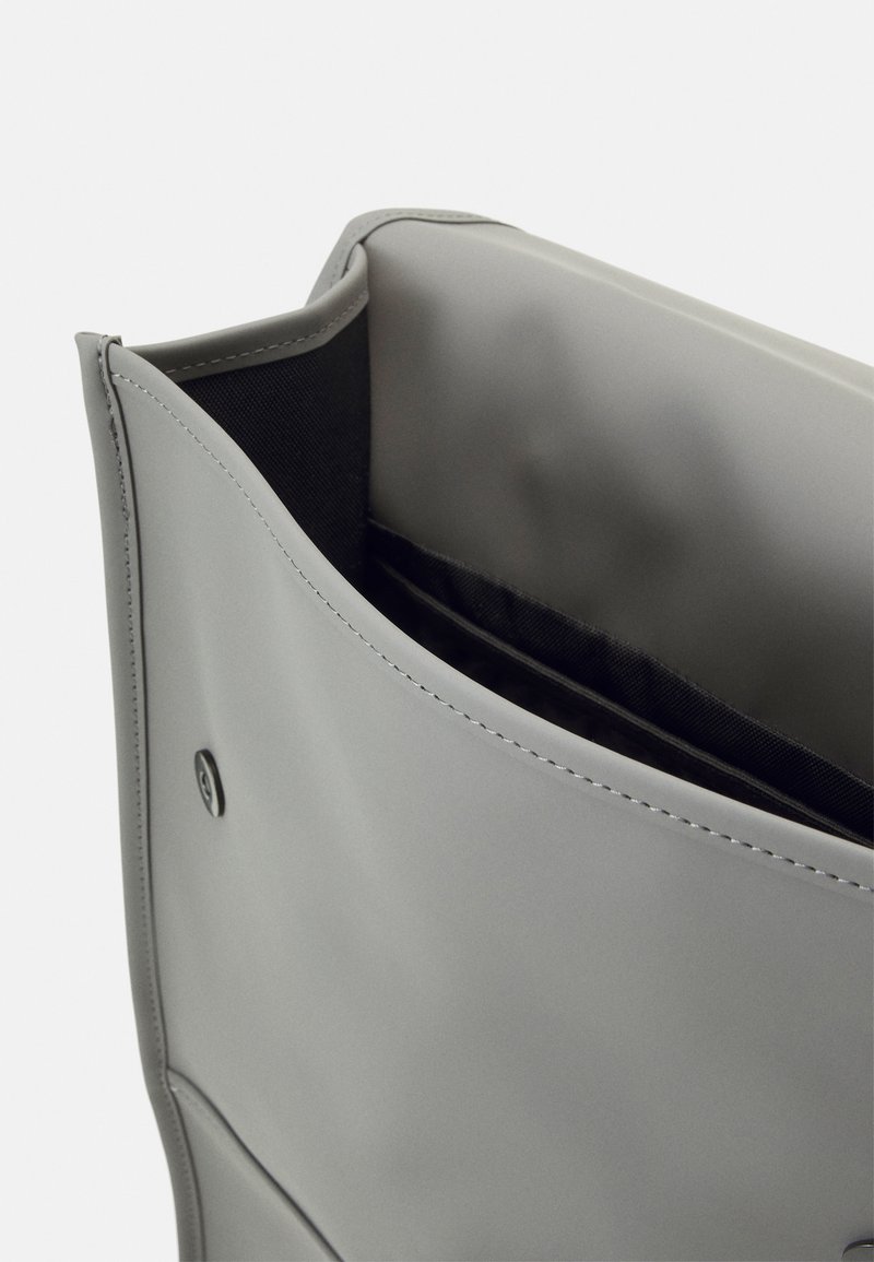 Sac en simili cuir gris clair avec une texture douce, ouvert sur le dessus, et doublure intérieure noire. Présente un logo discret et des bords bien cousus.