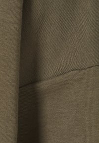 Tessuto verde oliva con un motivo strutturato a righe. Primo piano che mostra le variazioni nella tessitura e nella profondità del colore su due segmenti.