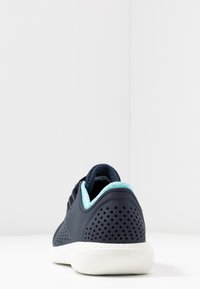 Chaussure de sport bleu marine en matériau perforé, accents turquoise, col rembourré et semelle blanche, vue de dos.