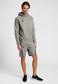 Ensemble sweat à capuche gris et shorts avec accents noirs. Présente une finition texturée, un logo sur la poitrine et des bandes latérales le long des shorts.