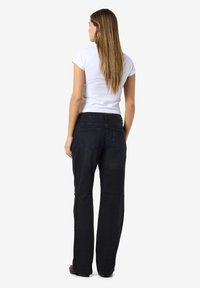 Zwarte denim jeans met een rechte snit en twee achterzakken. Gecombineerd met een witte getailleerde t-shirt, gezien van de achterkant.