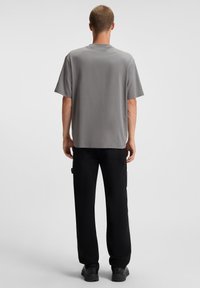 Gray short-sleeve t-shirt with a relaxed fit, featuring a crew neckline. Paired with black cargo pants and black footwear.