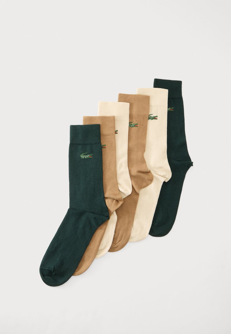 Six paires de chaussettes vertes, beiges et crème disposées côte à côte, chacune avec un petit logo crocodile brodé près du haut.