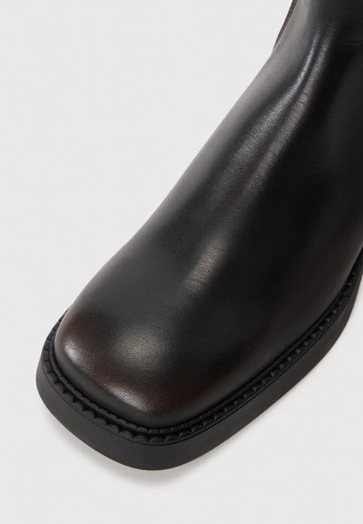 Black leather ankle boot with a rounded toe, smooth texture, and a sturdy rubber sole featuring a stitched accent around the edge.