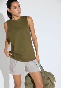 Top senza maniche verde oliva con scollatura rotonda, abbinato a pantaloni corti grigio chiaro e una borsa verde oliva coordinata, con tasche cargo.
