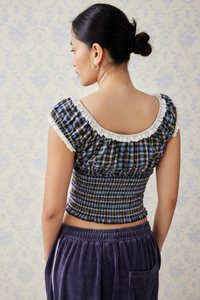 Plavi i žuti karirani kratki top s naboranim bijelim izrezom, naboranom teksturom i kratkim napuhanim rukavima, u kombinaciji s ljubičastim baršunastim hlačama.