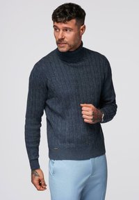 Pull en tricot marine avec un col haut et un motif en câble texturé. Il dispose de longues manches et d'une petite accentuation de marque à l'ourlet.