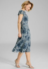 Robe midi plissée bleue avec des manches courtes à volants, en tissu léger avec un motif tie-dye. Talons argentés à lanières.