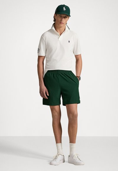 Biała koszulka polo z kołnierzykiem, zielone szorty i białe trampki. Zielona czapka z logo. Prosty design, codzienny krój i minimalne detale.