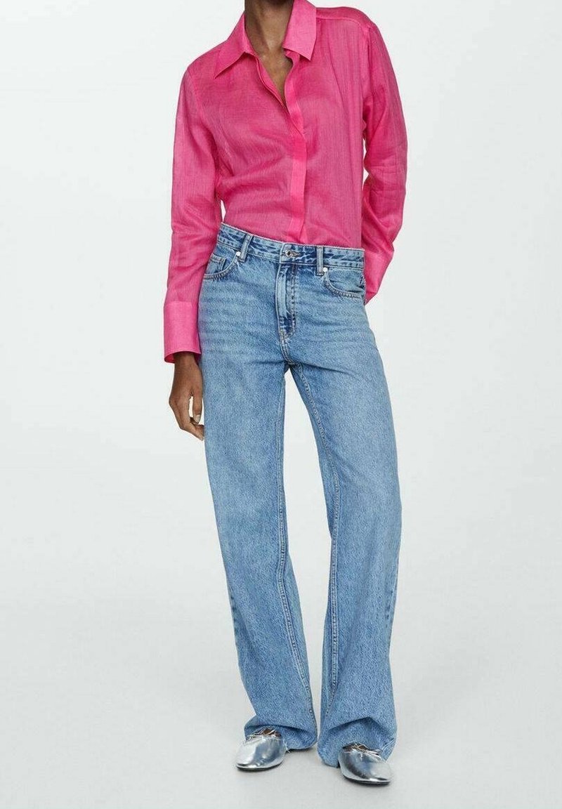 Personne portant une chemise rose vif à manches longues rentrée dans un jean taille haute, bleu clair, à jambes larges, et des chaussures argentées.