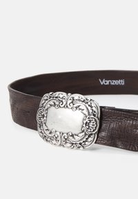 Cinturón de cuero marrón con un acabado texturizado y una hebilla de metal en tono plateado decorativa, que presenta diseños florales y una sección central en blanco.