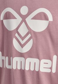 Hvid geometrisk bi-logo og delvist "hummel" tekst på tekstureret pink stofbaggrund.