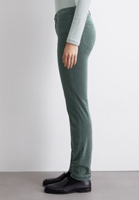 Groene broek in een slim fit ontwerp met een gladde textuur. Voorzien van achterzakken en een mid-rise taille. Draagt met zwarte instapschoenen.