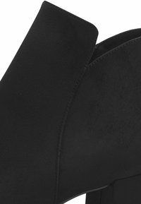 Black suede ankle boot with a smooth texture, contoured shape, and a chunky heel. Features a clean, minimal design and stitched accents.