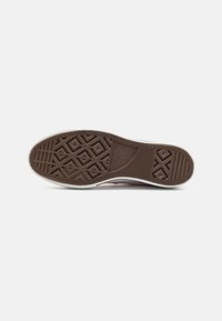 Rubber shoe sole with a brown textured pattern featuring geometric shapes and branding. Edges are white, providing contrast with the brown.