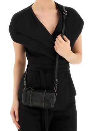 Borsa a tracolla in pelle nera di forma cilindrica, con borchie metalliche decorative, tracolla corta e texture liscia, indossata su un abbigliamento scuro.