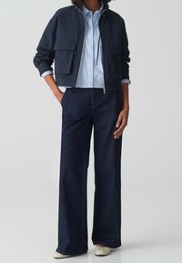 Marinblå kort jacka med två framfickor, ljusblå randig skjorta under, och vida mörk denimbyxor. Off-white skor fulländar looken.