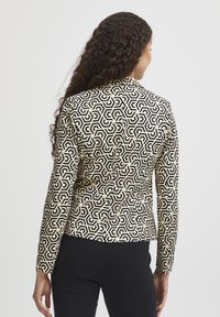 Blazer noir et crème à motif géométrique, coupe ajustée, manches longues et texture lisse. Détails de couture visibles.