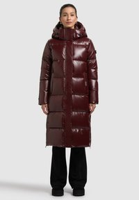 Bordó színű, fényes felületű pufi kabát, kapucnival, hosszú ujjal és egyenes szabással. Vastag, steppelt részek a szigeteléshez.