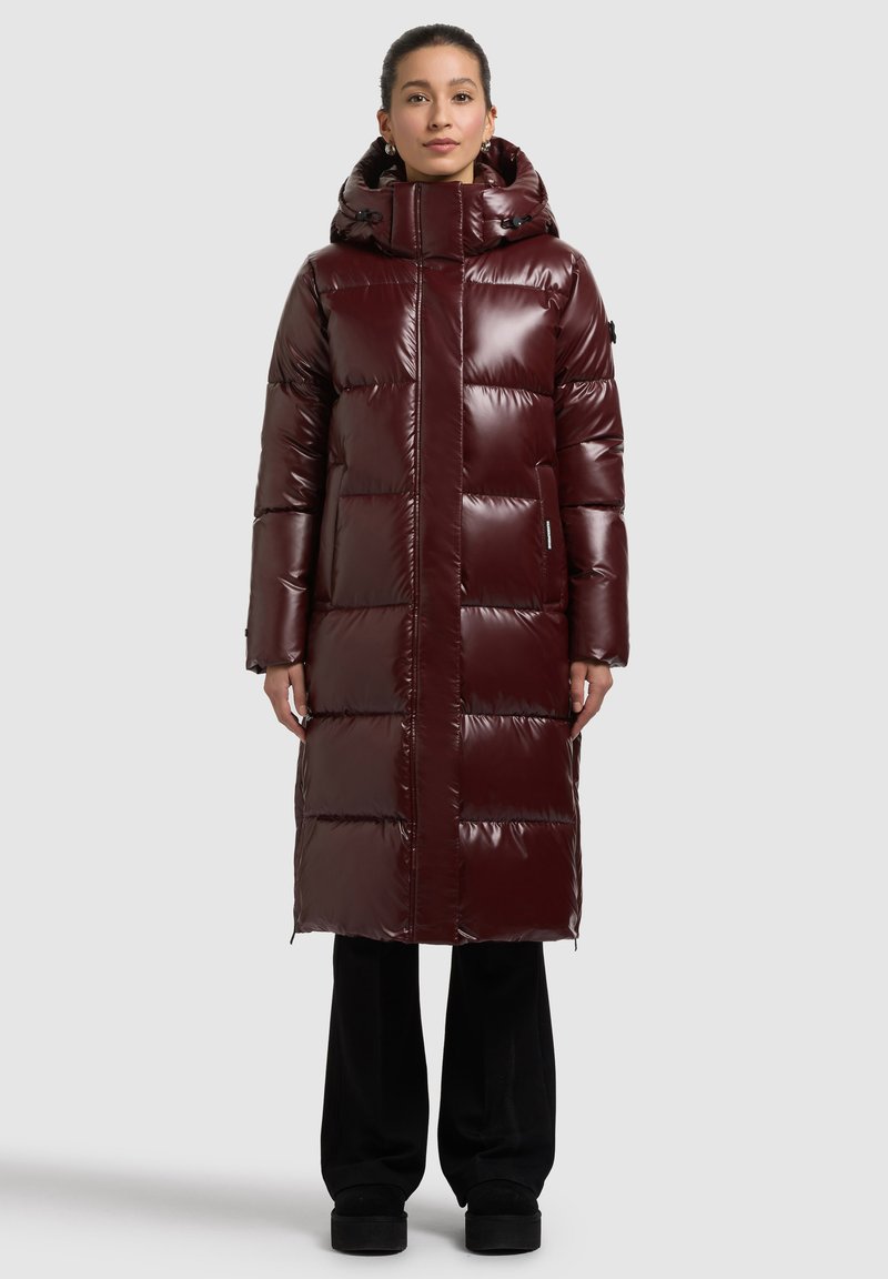 Bordó színű, fényes felületű pufi kabát, kapucnival, hosszú ujjal és egyenes szabással. Vastag, steppelt részek a szigeteléshez.