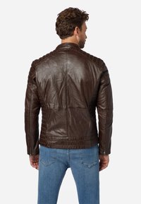 Brun läderjacka med quiltade axelpartier, figurnära design och dragkedjeslutningar. I kombination med ljusblå jeans.