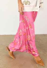 Κάτω μέρος σώματος γυναίκας που φοράει φωτεινό ροζ φούστα με πολύχρωμα σχέδια, μαύρα μυτερά τακούνια με καρφιά και λευκό πλεκτό πουλόβερ με κέντημα.