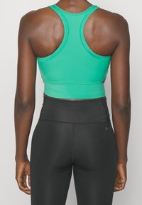 Zelený sportovní crop top s designem na zádech, hladkým povrchem a šitými švy, doplněný o černé legíny s vysokým pasem.