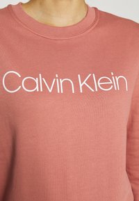 Felpa rosa con logo "Calvin Klein" bianco. Realizzata in tessuto morbido, presenta un collo a giro e polsini a coste, progettata per un fit rilassato.