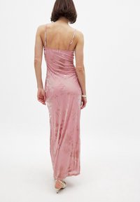 Lange roze satijnen jurk met spaghettibandjes, bloemenpatroon en een vloeiende silhouet. Heeft een zachte glans en een rechte zoom.