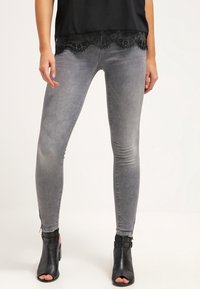 Jeans ajustados de mezclilla gris con una cintura de altura media, que presentan una textura suave y un ligero desgaste, combinados con una blusa negra con encaje.