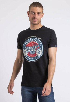 T-shirt en coton noir avec un col rond, arborant un graphique de moto coloré et du texte en rouge, blanc et bleu. Coupe standard avec des manches courtes.